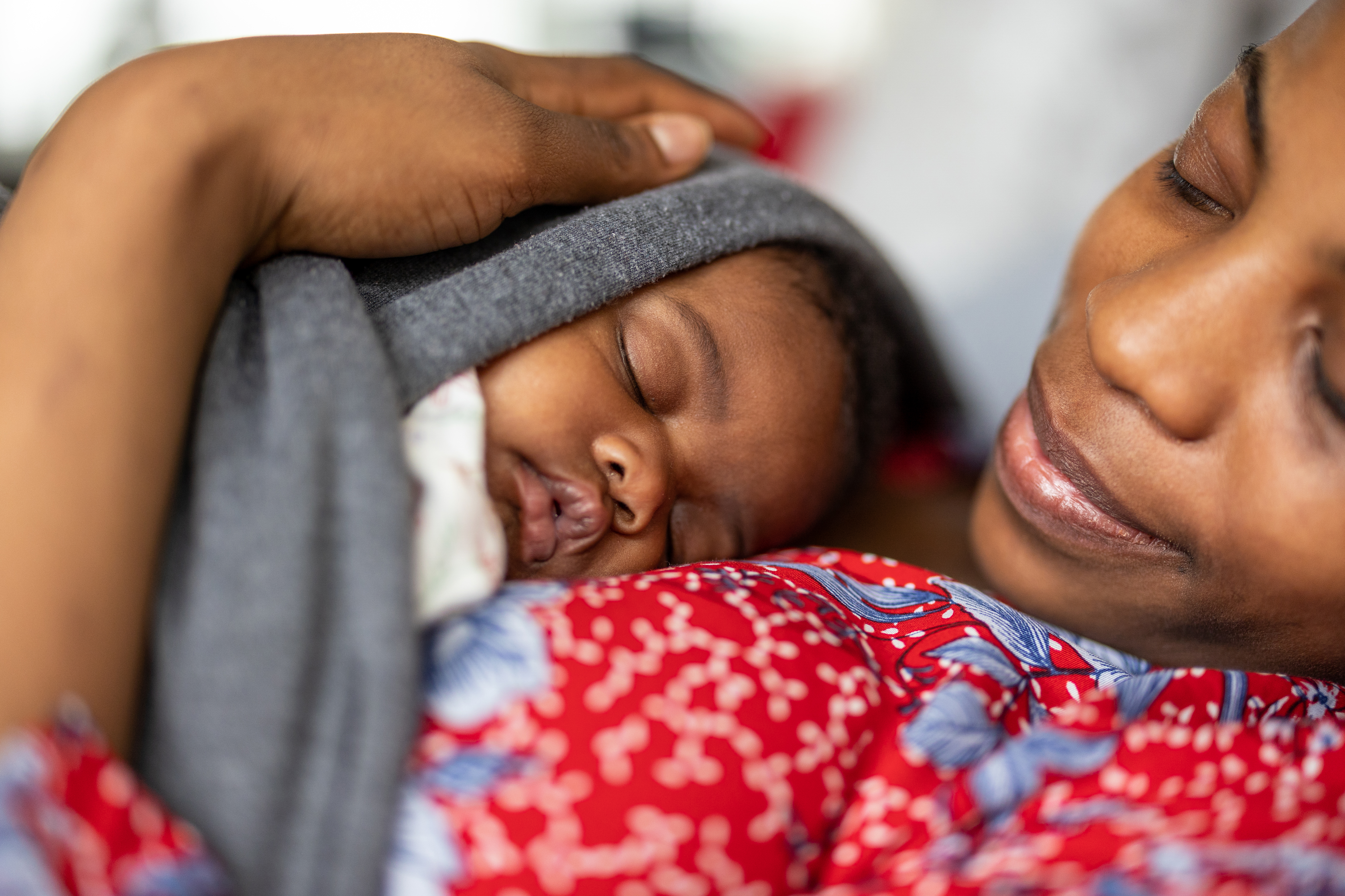 A mother holds her newborn baby closely on her chest, while the baby sleeps.