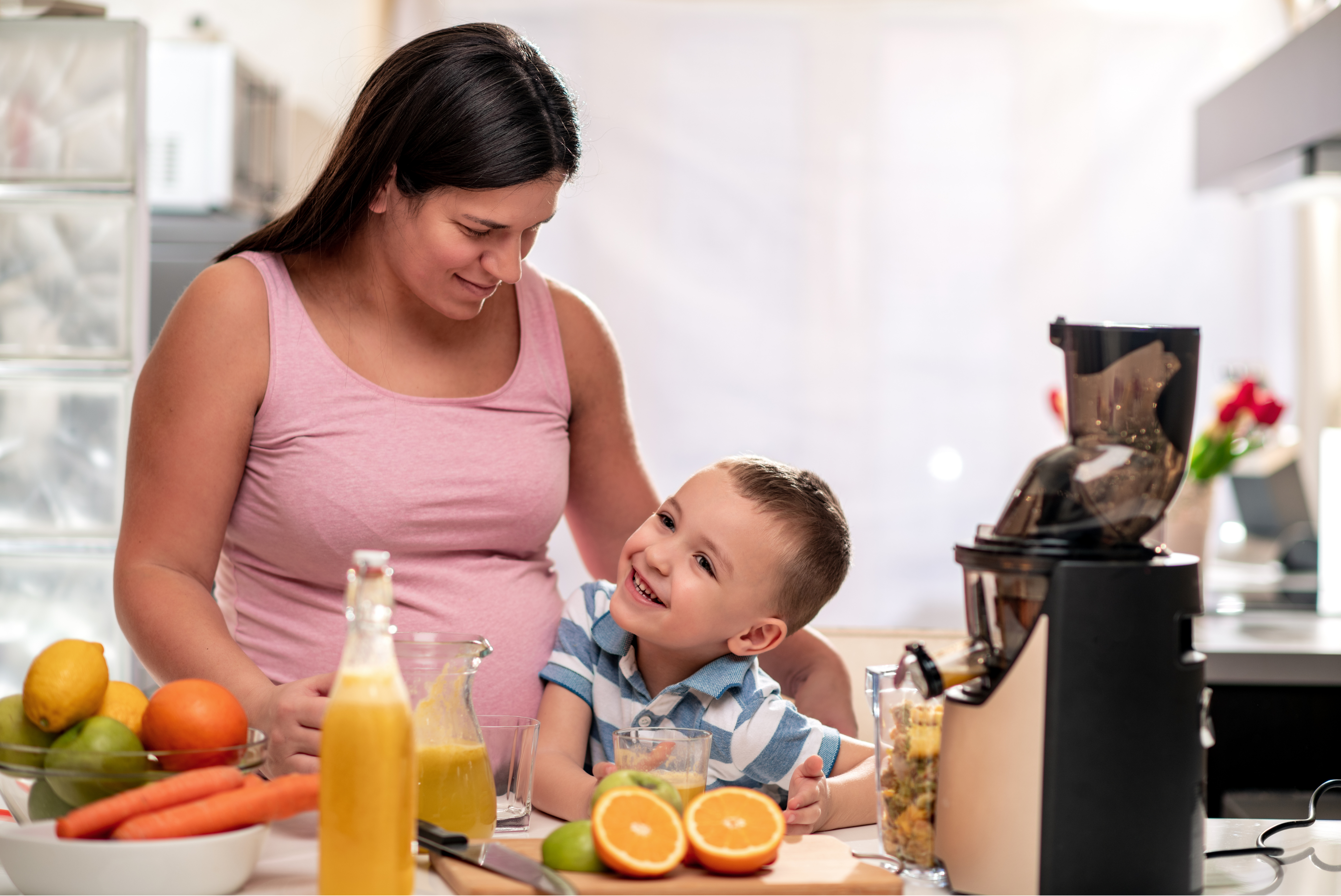 A pregnant person laughs with a family member in their home kitchen.