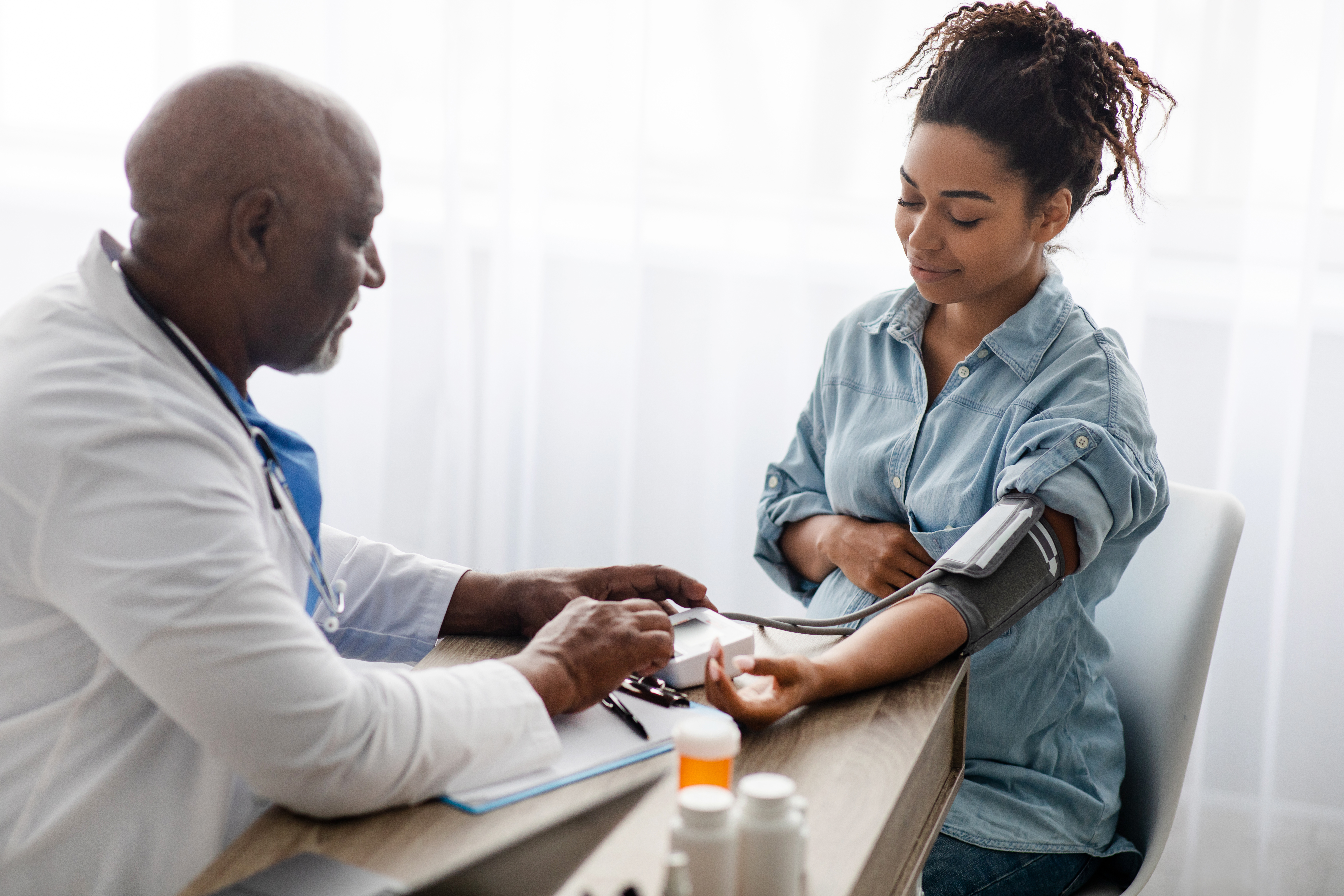 A pregnant person has their blood pressure read by a doctor
