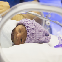 A caregiver prepares equipment for a NICU patient in an incubator.