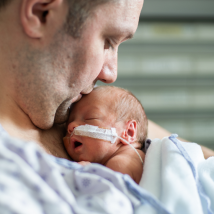 A NICU baby receives a kiss on the head from its parent.