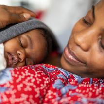 A woman holds her sleeping newborn baby closely on her chest.
