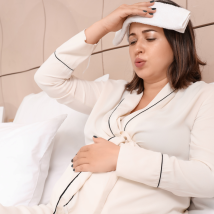A pregnant person with a fever is sitting in bed at home.