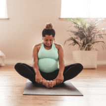 A pregnant person does yoga in a sunny room.