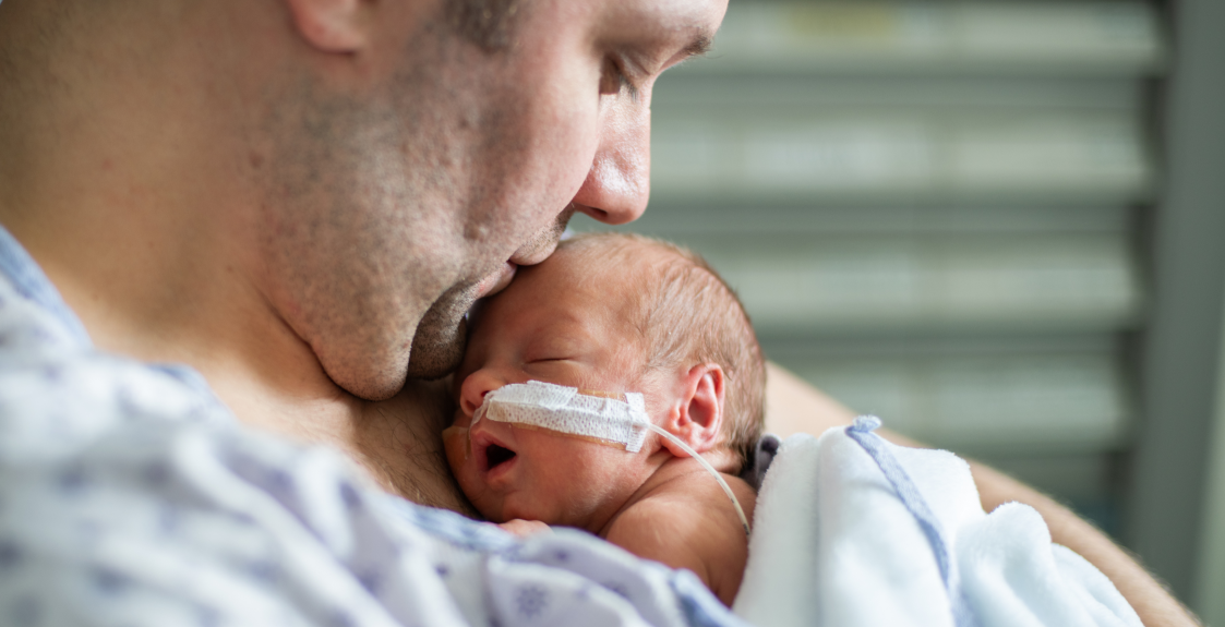 A NICU baby receives a kiss on the head from its parent.