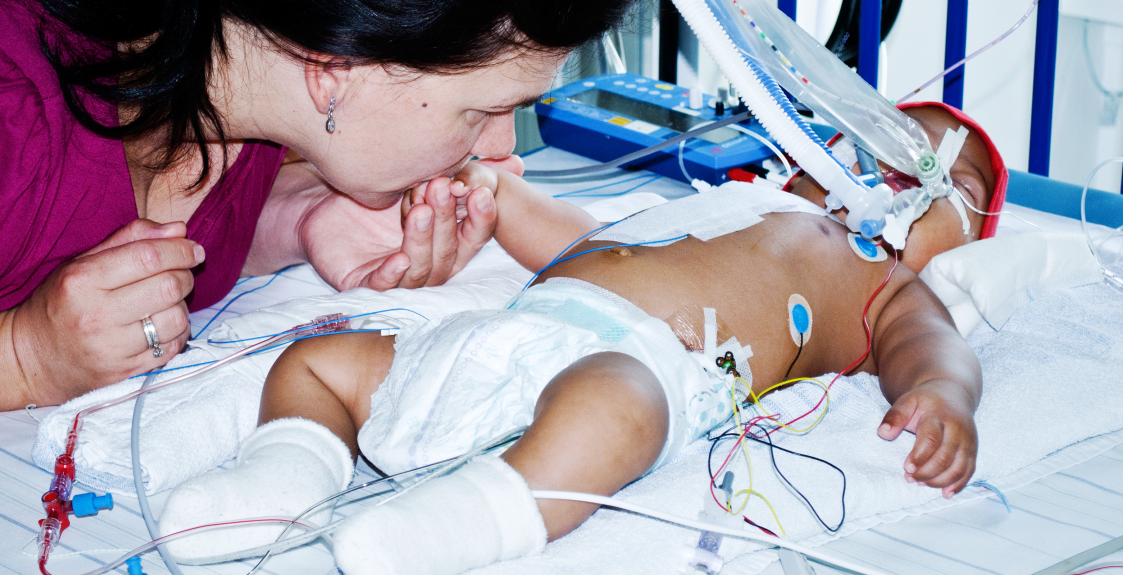 A NICU baby receives a kiss on the hand from its parent.