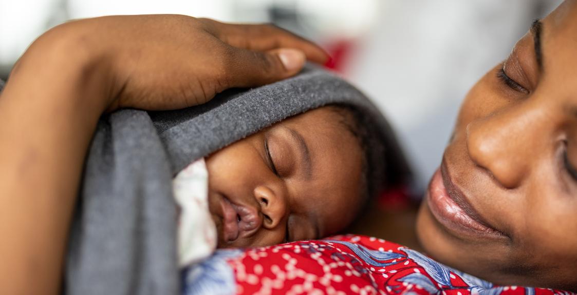 A woman holds her sleeping newborn baby closely on her chest.