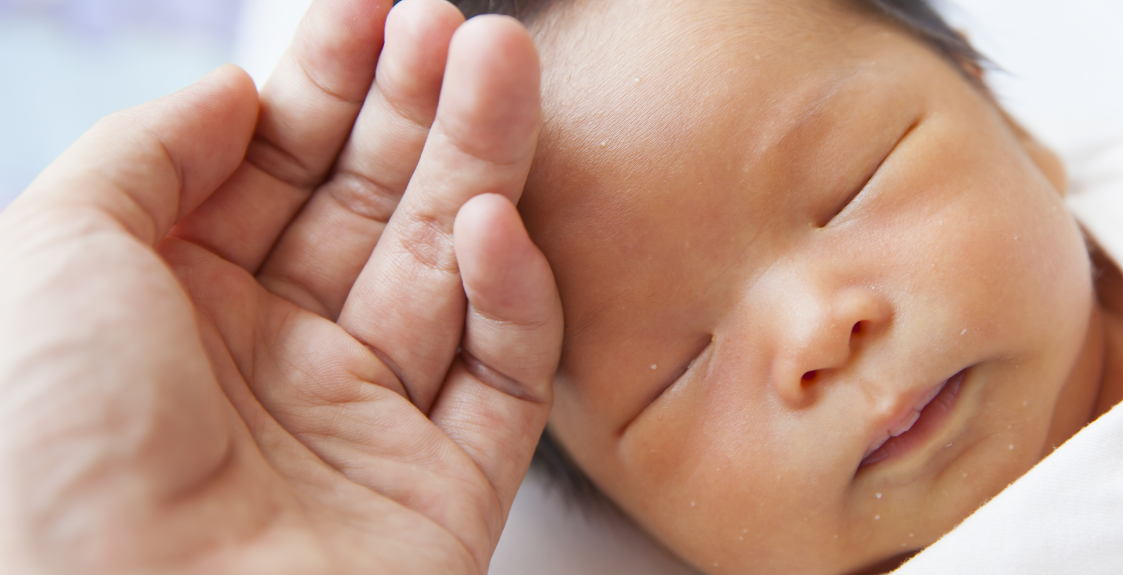 A NICU caregiver places their hand on a NICU baby's forehead.